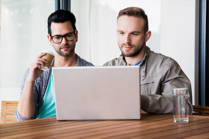 Focused gay couple using laptop outdoors