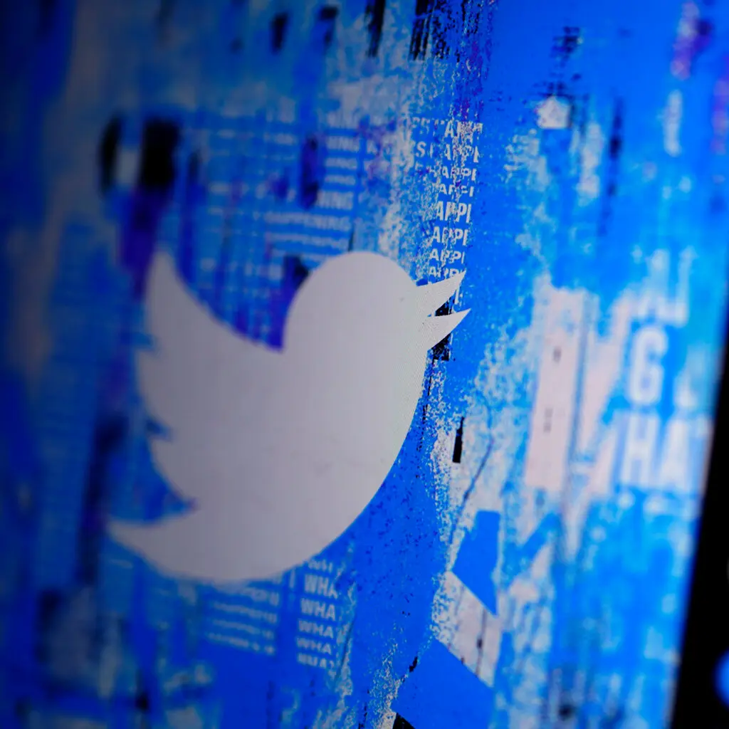 A screen showing Twitter's bird logo against blue digital noise is seen in shallow focus.