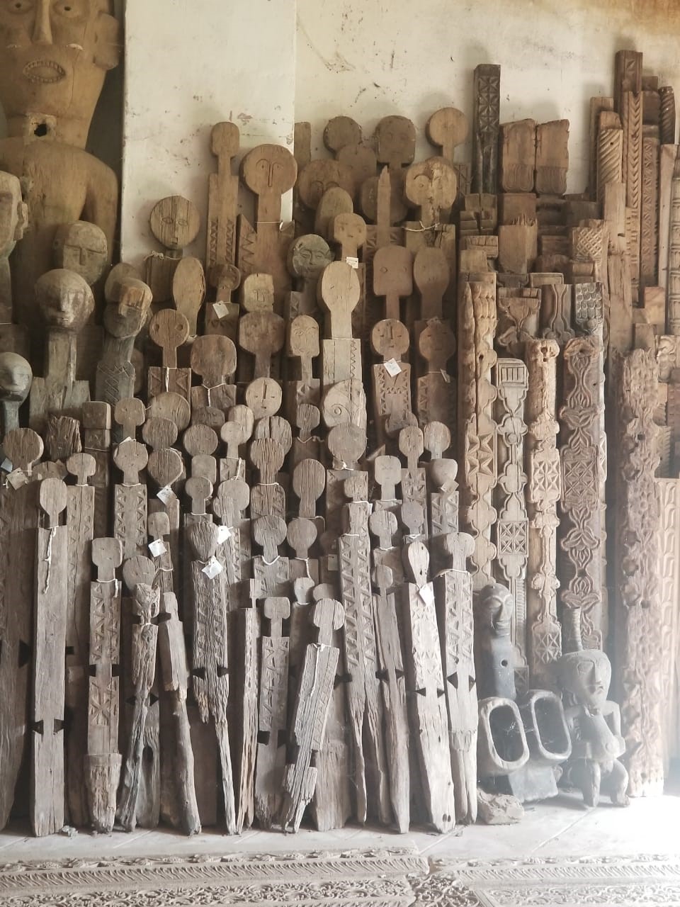 A collection of tall, thin wooden statues of different heights rests against a wall. A collection of tall, thin wooden statues of different heights rests against a wall.